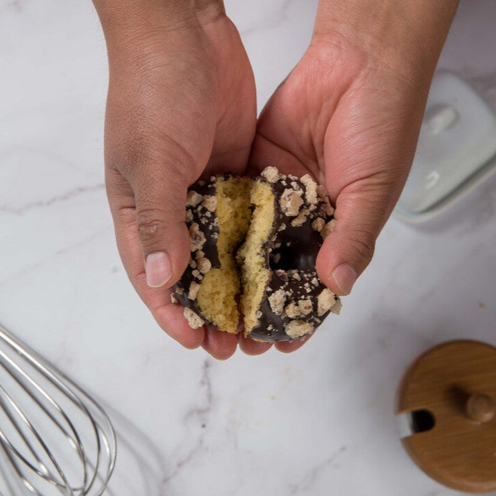 Hands holding a layered FITbelly donut with chocolate and cream on a marble surface.