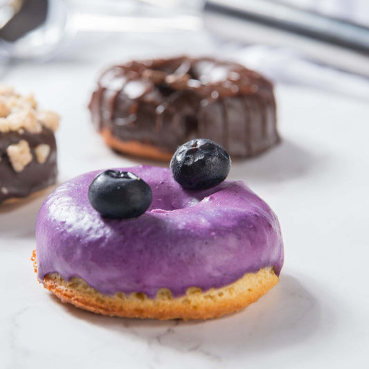 Purple frosted FITbelly keto donut with blueberries on a white surface