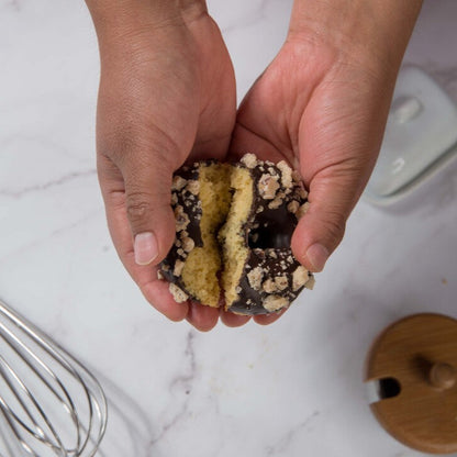 Hands holding a layered FITbelly donut with chocolate and cream on a marble surface.