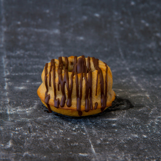 FITbelly keto donut with chocolate drizzle on a textured dark surface