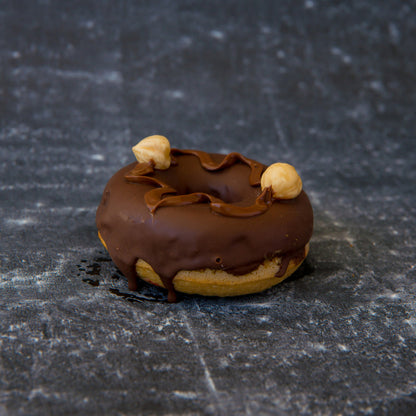 Chocolate-glazed FITbelly donut with nuts on a textured black surface