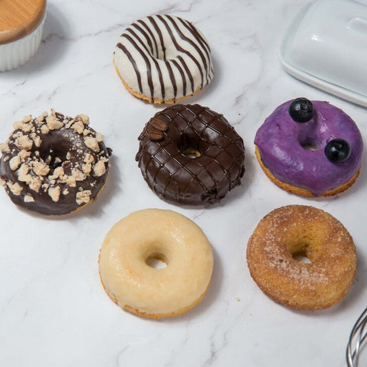 Assorted FITbelly donuts on a marble surface with a whisk in the background