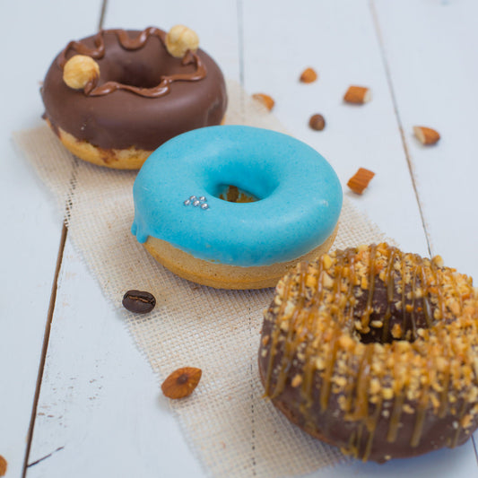 Three FITbelly donuts with different toppings on a light wooden surface